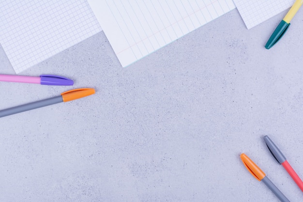 Чистые листы бумаги и разноцветные карандаши на сером.