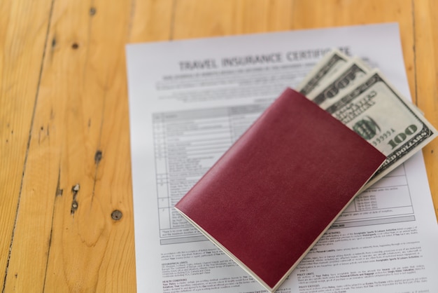 旅行航空保険申込書の上に木製のテーブルに米ドルの空白のパスポート。