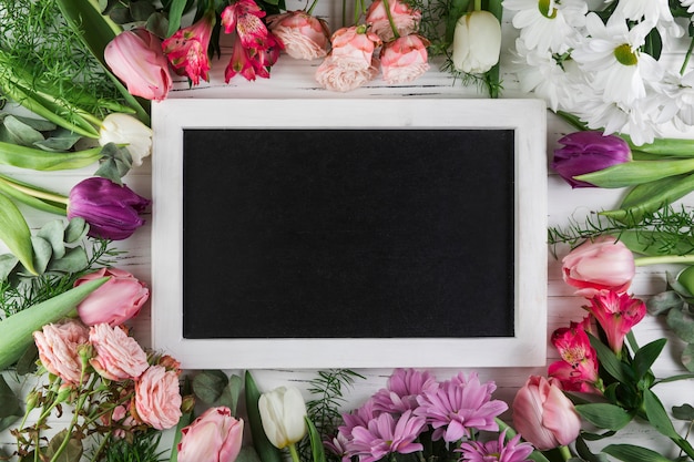 Blank rectangular slate surrounded with rose; tulip; chamomile and alstroemeria flowers