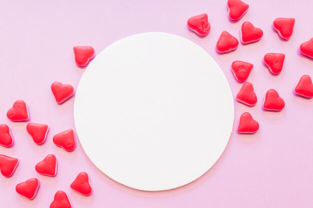 Blank round frame decorated with red heart shape candies on pink background