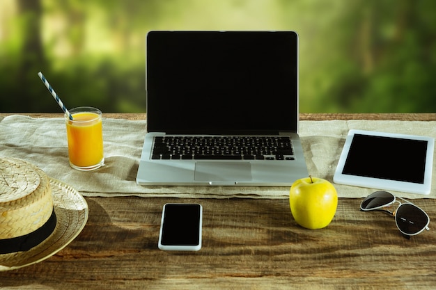 Free photo blank screens of laptop and smartphone on a wooden table outdoors with nature on wall fruits and fresh juice nearby. concept of creative workplace, business, freelance. copyspace.