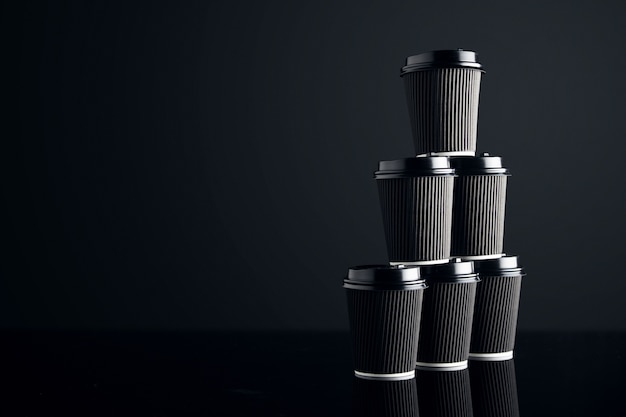 Пустой набор черных картонных бумажных стаканчиков на вынос, закрытых крышками в форме пирамиды, представлен справа