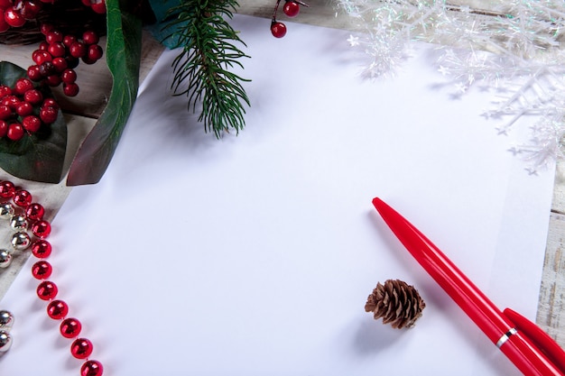 чистый лист бумаги на деревянном столе с ручкой и рождественскими украшениями.