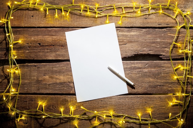 Free photo blank sheet of paper on the wooden table with a pen and  christmas decorations.