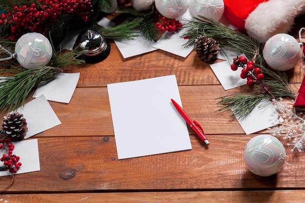 blank sheet of paper on the wooden table with a pen and Christmas decorations.