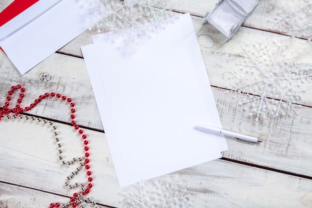 The blank sheet of paper on the wooden table with a pen and Christmas decorations.