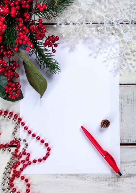 The blank sheet of paper on the wooden table with a pen and Christmas decorations.