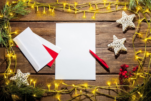 The blank sheet of paper on the wooden table with a pen and Christmas decorations.