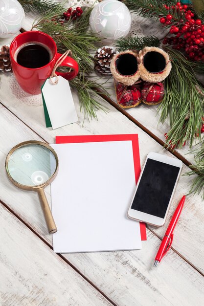 blank sheet of paper on wooden table with a pen, phone and Christmas decorations