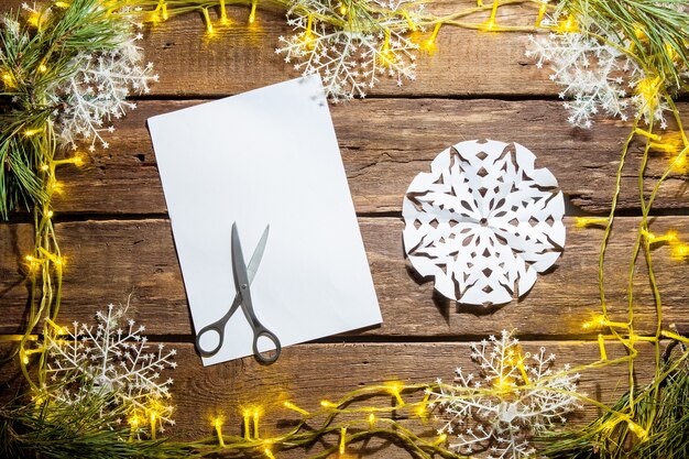 The blank sheet of paper on the wooden table with a scissors and Christmas decorations.