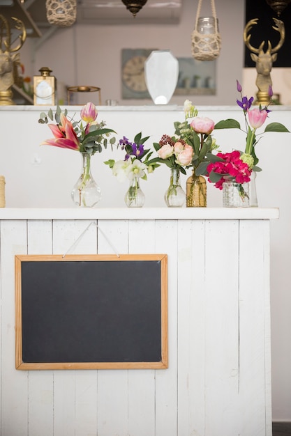 Чистый сланец висит на стене с красивыми вазами для цветов в цветочном магазине