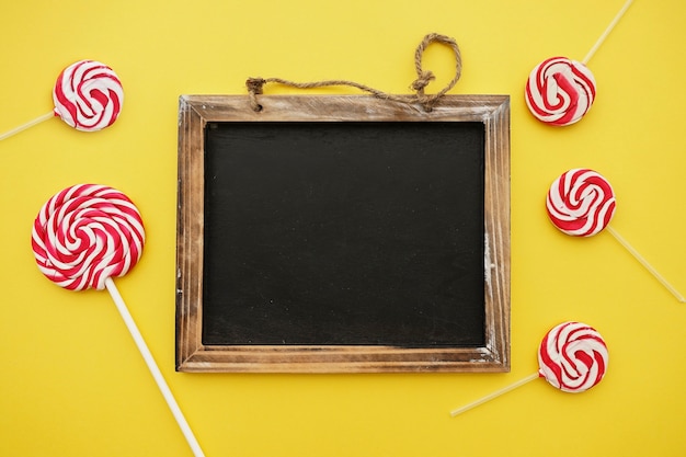 Blank slate and lollipops on yellow background