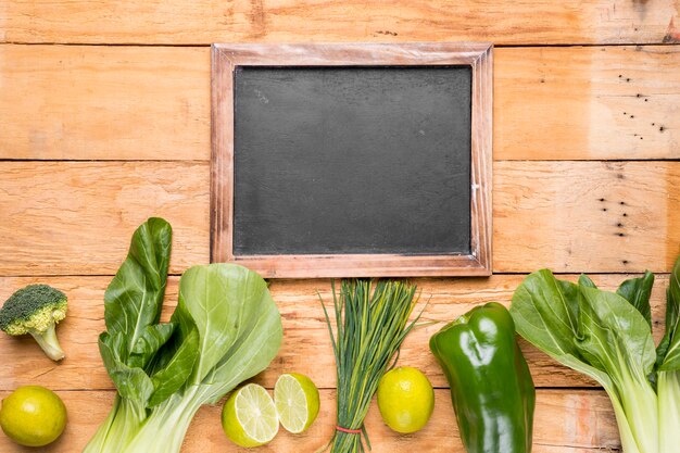 Blank slate with row of bokchoy; broccoli; lemon; bell pepper; chives on wooden desk