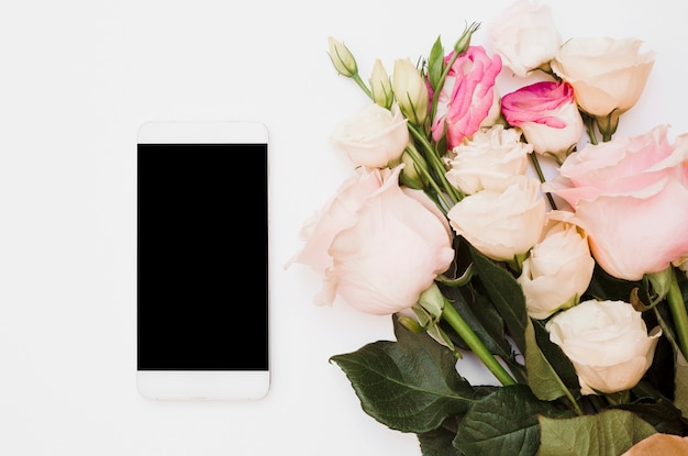 Blank smartphone with flower bouquet on white backdrop