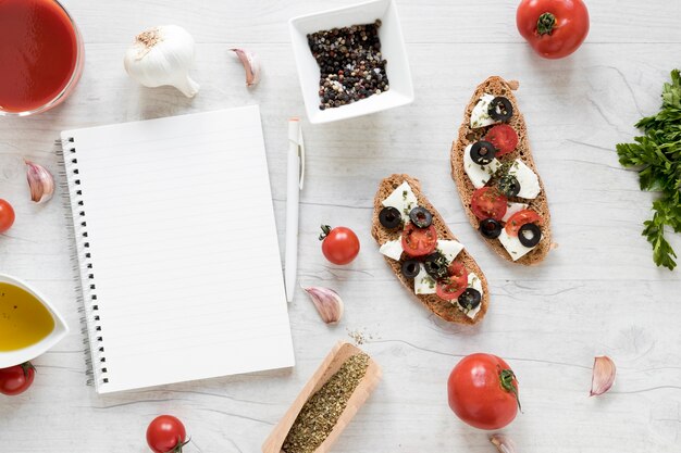 Blank spiral diary and bruschetta with ingredient on wooden table