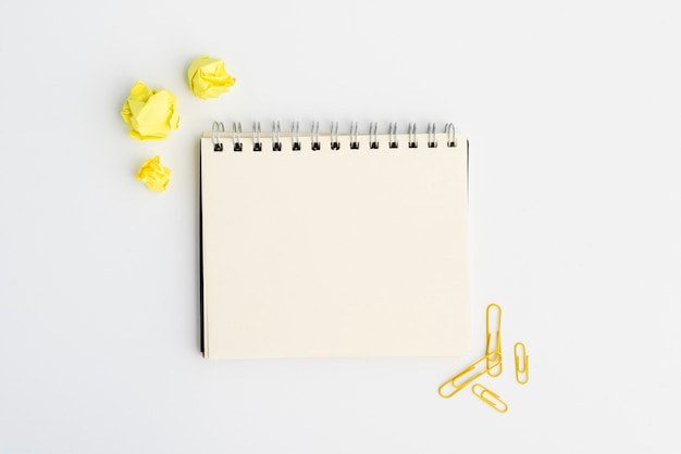 Blank spiral diary with yellow crumpled paper and paperclip over white background
