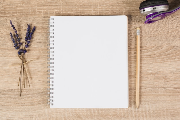 Blank spiral notebook; pencil; headphone and lavender twigs on wooden background