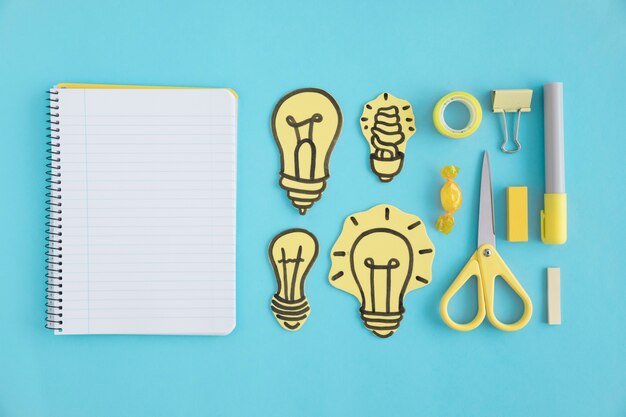 Blank spiral notebook with paper light bulbs and stationery on blue background