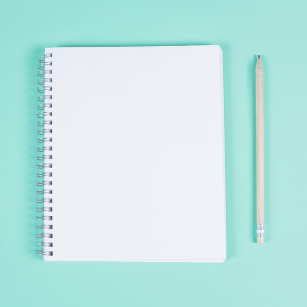 Free photo blank spiral notebook with pencil on turquoise background