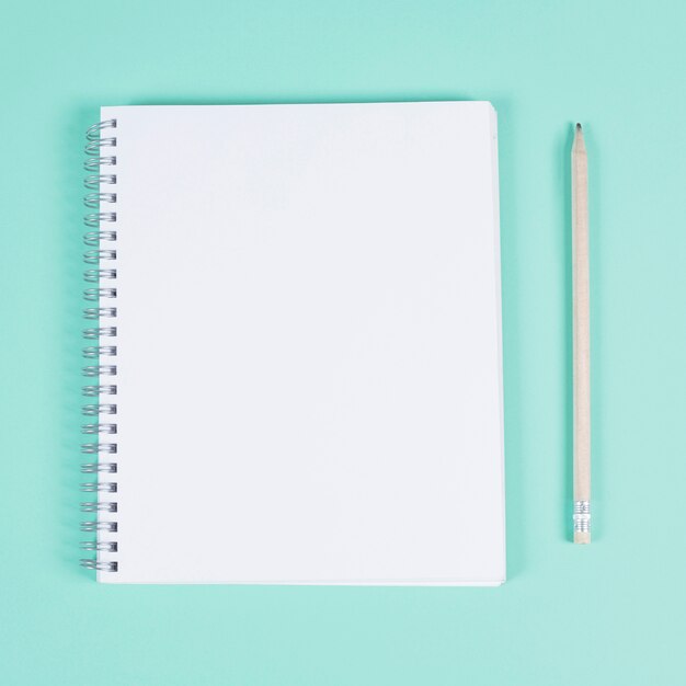 Blank spiral notebook with pencil on turquoise background