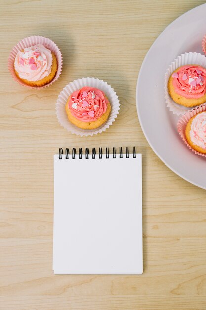 Blank spiral notepad; cupcake over wooden desk