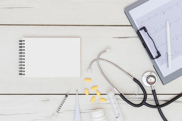 Free photo blank spiral notepad; medical equipment's; stethoscope and ecg report on clipboard over the wooden desk