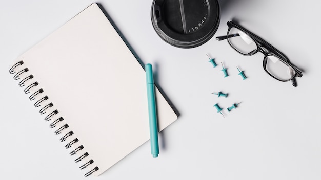 Blank spiral notepad; pen; coffee cup; eyeglasses and pushpins on white background