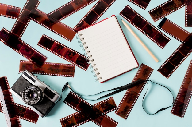 Free photo blank spiral notepad; pencil and camera with negative stripes on blue backdrop