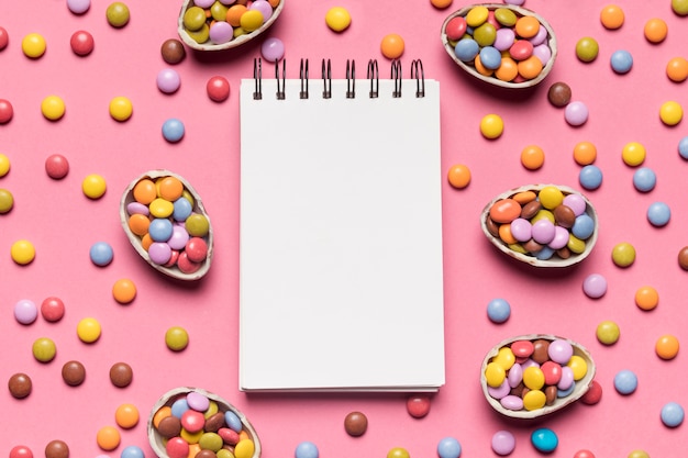 ピンクの背景にカラフルな宝石キャンディーに囲まれた空白のスパイラルメモ帳