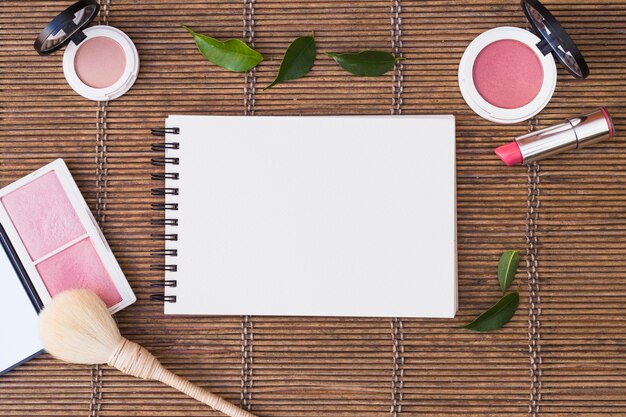 Blank spiral notepad surrounded with cosmetics products on placemat