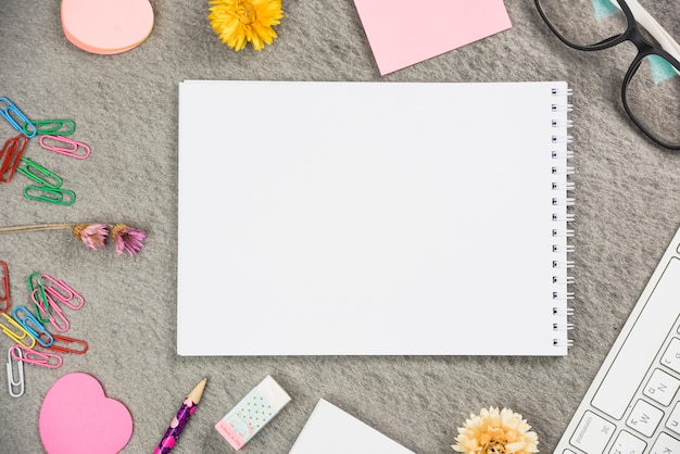 Blank spiral notepad surrounded with office supplies on gray backdrop