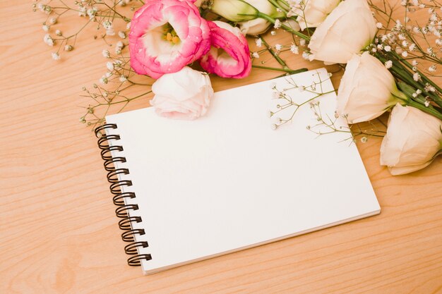 Blank spiral notepad with flower bouquet over wooden backdrop