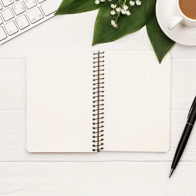 Free photo blank spiral notepad with keyboard,coffee cup and pen on white backdrop