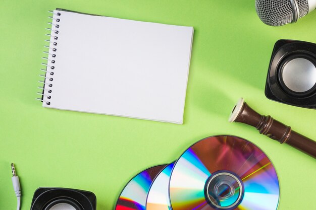 Blank spiral notepad with microphone; speaker; compact disc; block flute on green backdrop