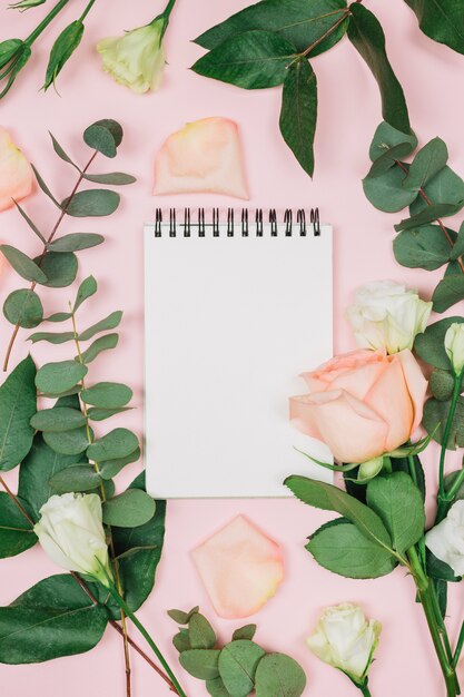 ピンクの背景に対してバラとトルコギキョウの花を持つ空白のスパイラルメモ帳