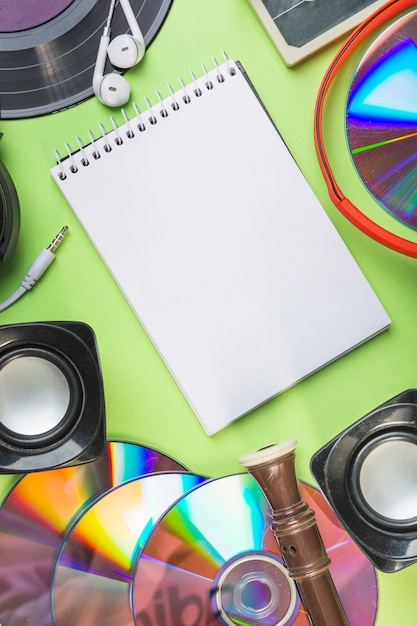 Blank spiral notepad with speaker; compact disc; block flute and earphone on green backdrop