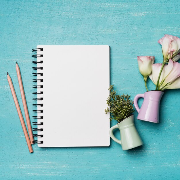 Blank spiral notepad with two pencils and vases on textured blue background