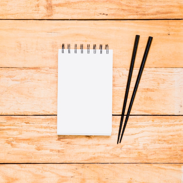 Blank spiral notepad with two wooden chopsticks over the wooden table