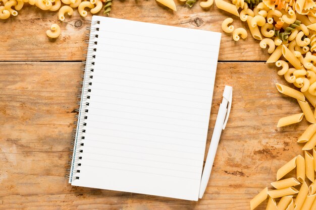 Blank spiral notepad with variety of raw pasta over table