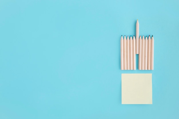 Blank sticky note with rows of colored pencil over blue background