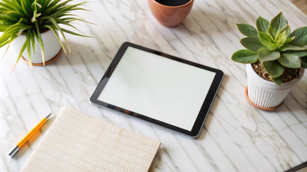 A blank tablet notebook pen and potted plants on a marble surface