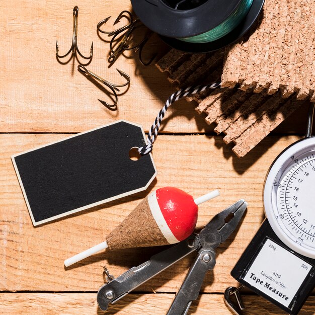 Blank tag; hooks; fishing float; pliers; corkboard; fishing reel and measuring tool on wooden desk