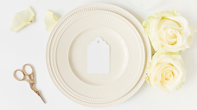 Blank tag on white plate with rose and scissor on white background