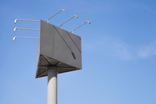 Blank triangular billboard pole with lights against blue sky