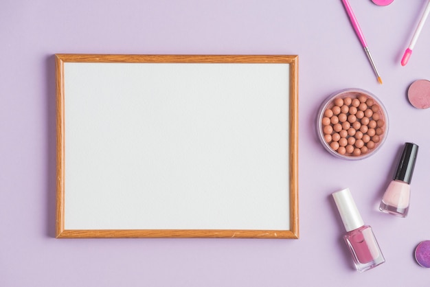 Пустая белая рамка с косметическими продуктами на фиолетовом фоне
