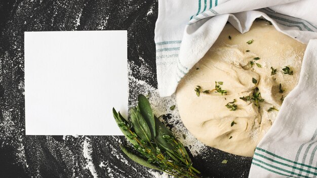 Blank white page and raw dough with rosemary on kitchen worktop