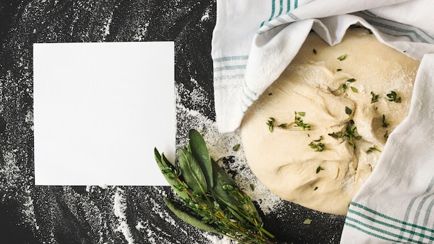 Blank white page and raw dough with rosemary on kitchen worktop