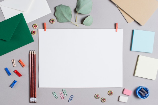 Blank white page with clothes peg surrounded with stationeries on gray background