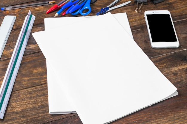 Blank white paper; cellphone and stationeries on wooden plank