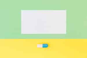 Free photo blank white paper and single capsule on green and yellow background